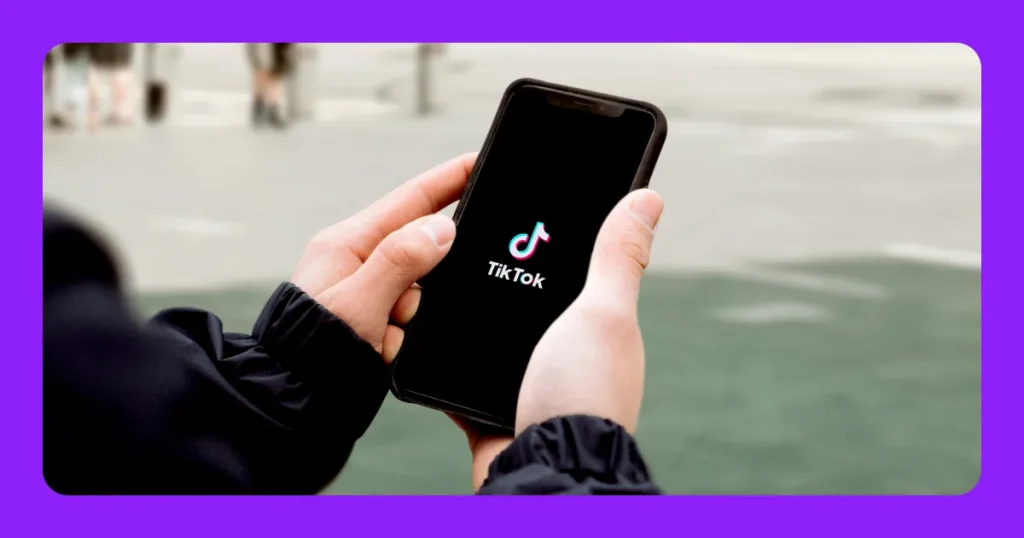 676050e70a1b5d2053b2c69f_A hand holding a phone with a screenshot of a black screen with the TikTok logo.