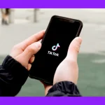 676050e70a1b5d2053b2c69f_A hand holding a phone with a screenshot of a black screen with the TikTok logo.